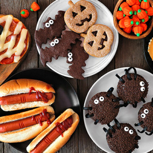 Halloween party food table scene over a rustic wood background. Overhead view. Spooky mummy pizzas, finger hot dogs, caramel apples, cupcakes, candy, cookies and donuts.